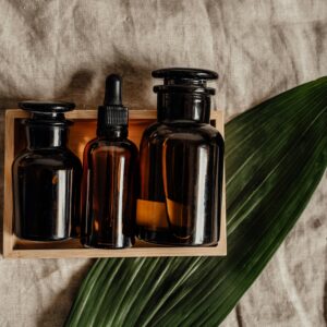Collection of brown glass bottles in a wooden box with a green leaf on burlap fabric, perfect for organic skincare themes.